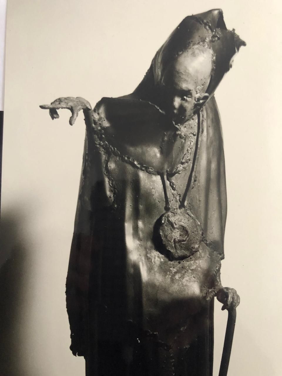 Figura encapuchada con medallón colgante y una mano en alto