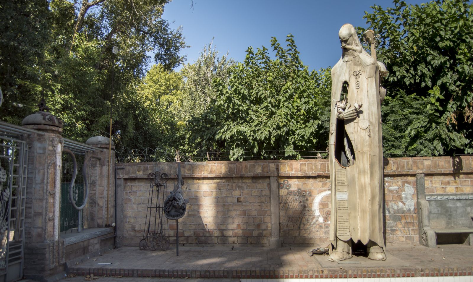 Patio de los Colosos, figura encapuchada junto al muro de ladrillo