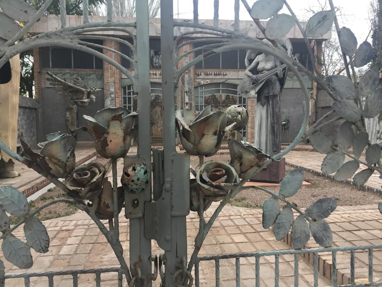 Portón de hierro forjado, detalle de las rosas forjadas con el ángel al fondo